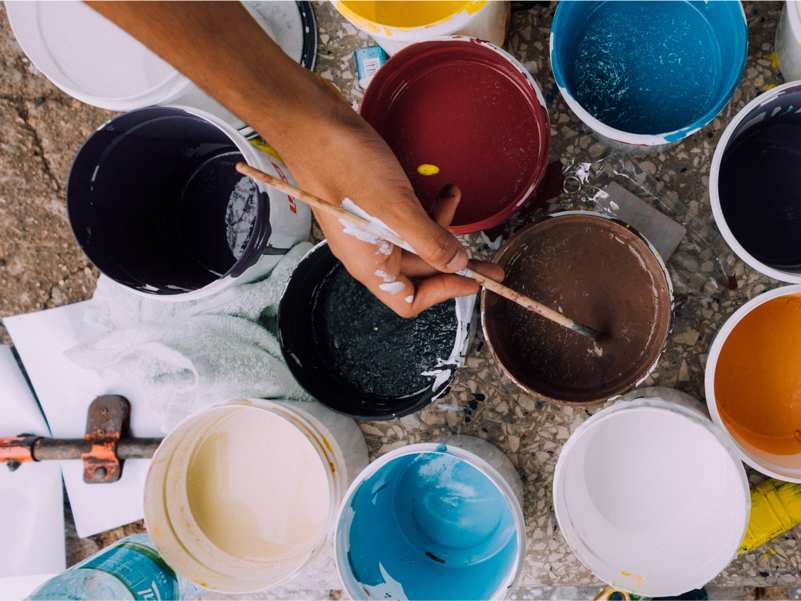 Buckets of paint with a hand holding a paintbrush.